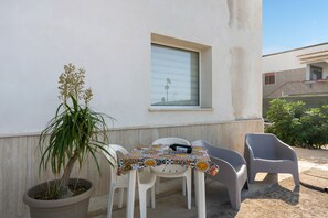 A small outdoor seating area with a table and chairs, a potted plant, and a window. - Apartment 'Josadè Rosso Corallo' with Sea View, Wi-Fi and Air Conditioning (Alcamo)