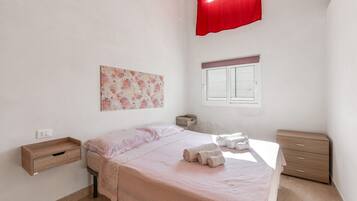 A bedroom with a bed, a bedside table, a window with a curtain, and a wall-mounted artwork.
