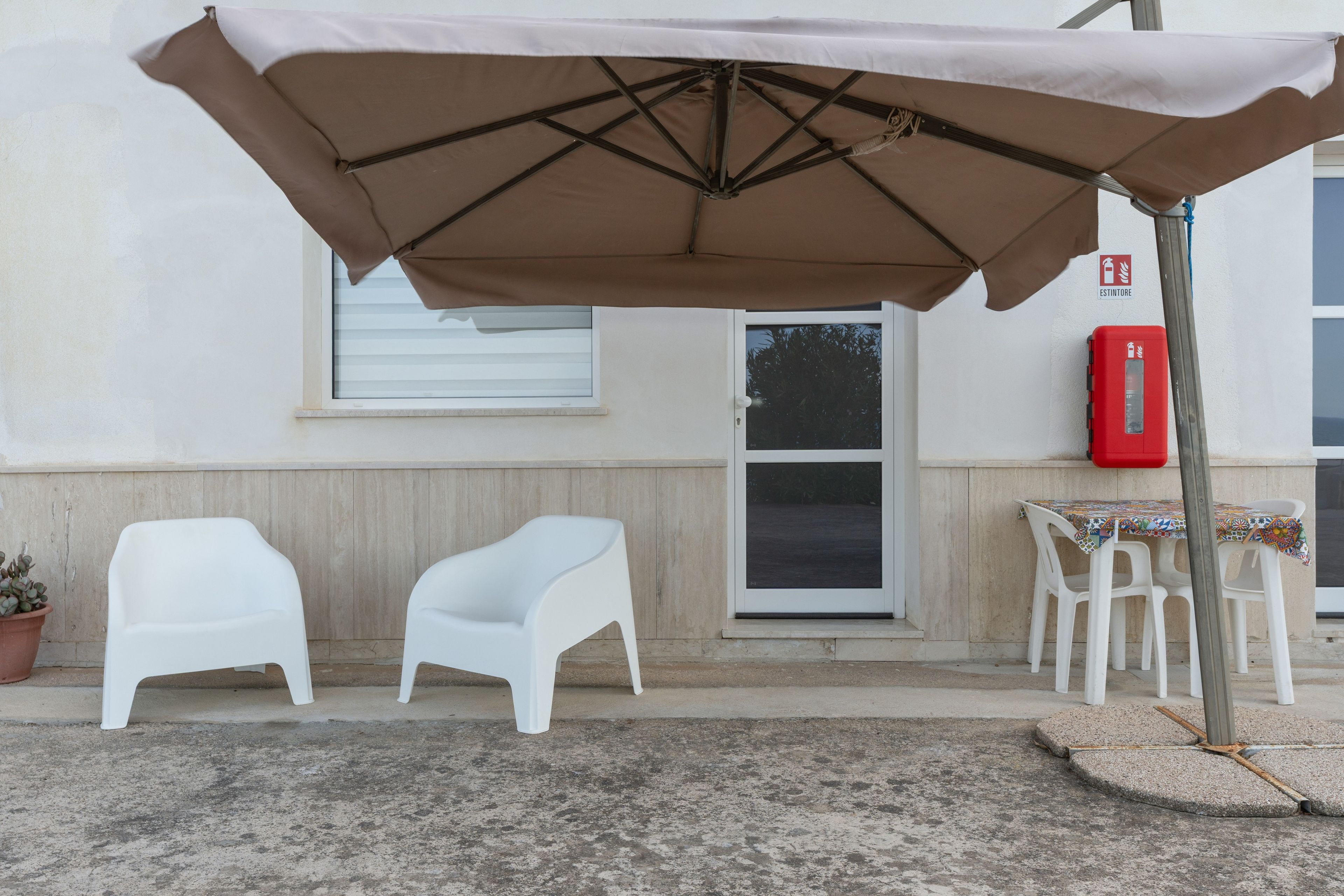 Een terras met een tafel en stoelen, een overdekte parasol en een brandblusser aan de muur.