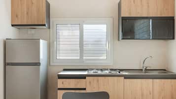 A compact kitchen with a refrigerator, stove, sink, and wooden cabinets.