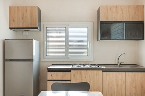 A compact kitchen with a refrigerator, stove, sink, and wooden cabinets. - Apartment 'Josadè Rosso Corallo' with Sea View, Wi-Fi and Air Conditioning (Alcamo)