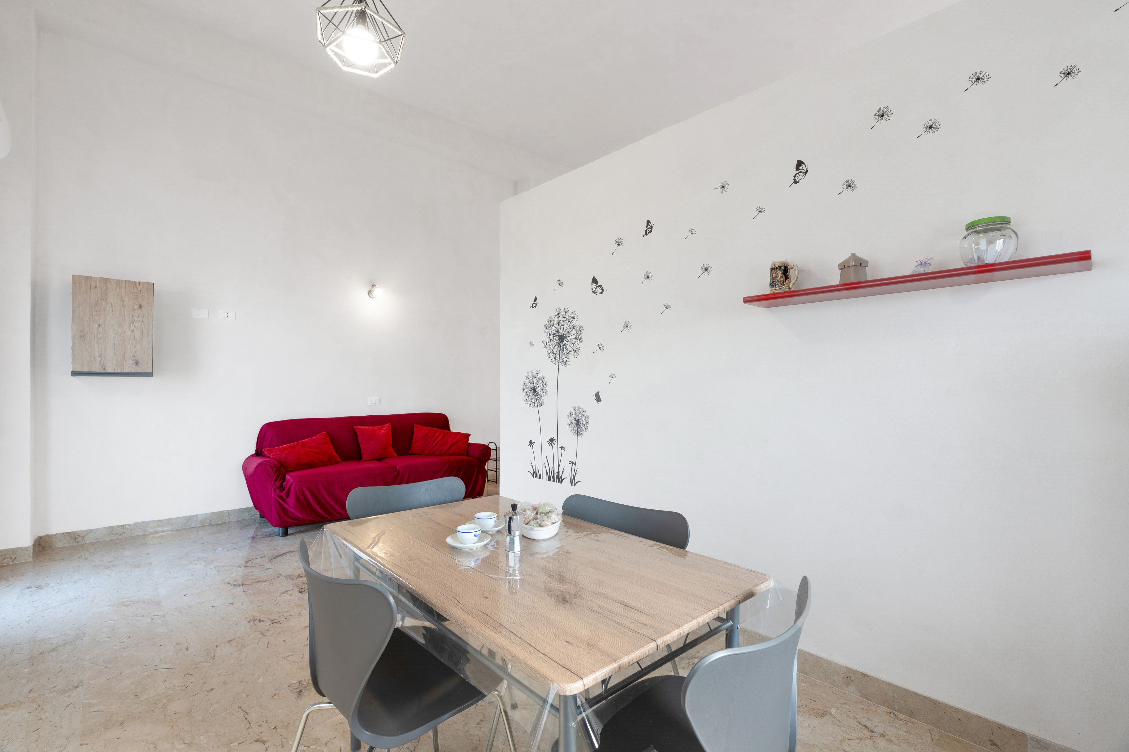 Un comedor con mesa de madera, sillas, un sofá rojo y una pared decorada con diseños de diente de león y mariposas.