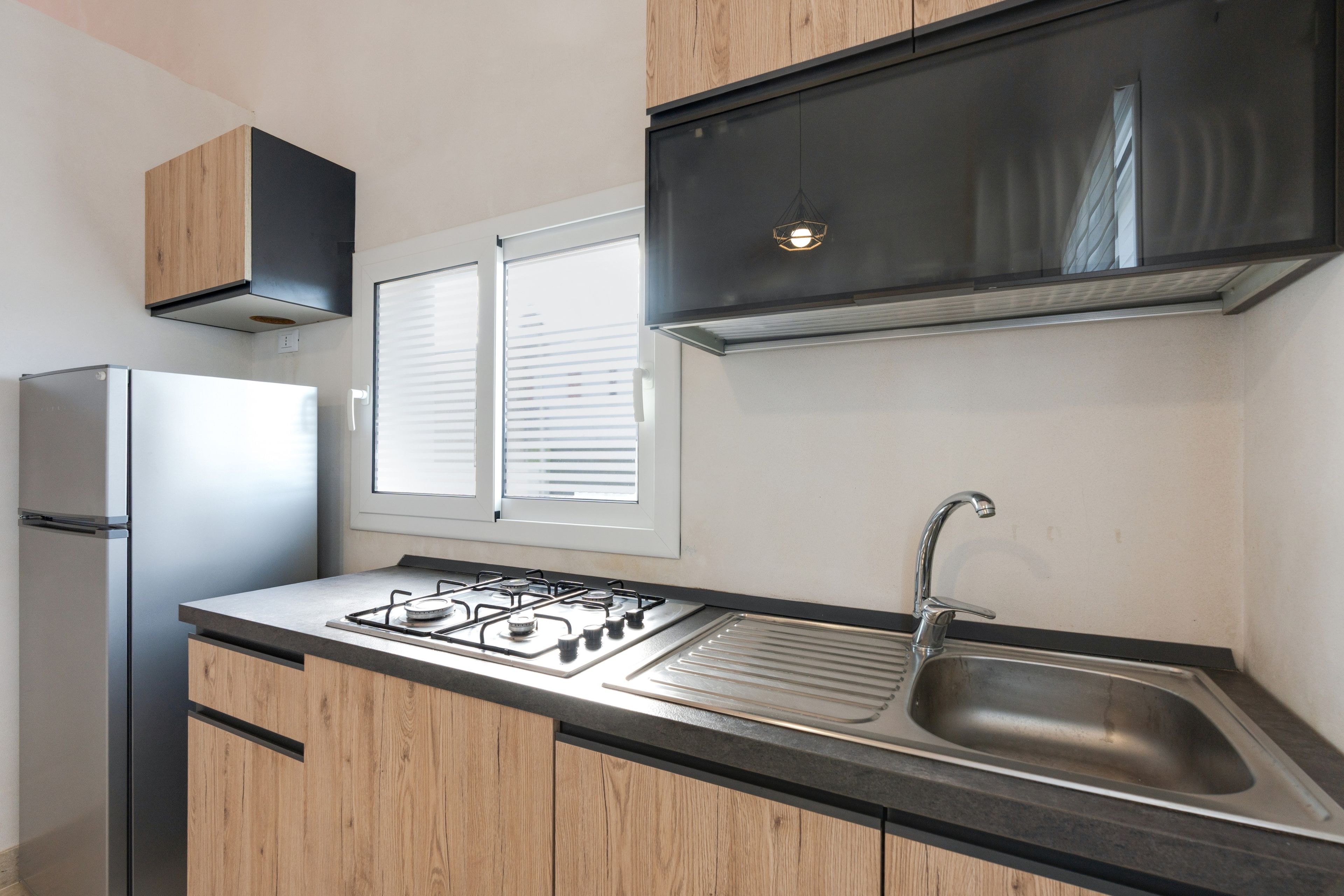 A modern kitchen with a stainless steel refrigerator, a gas stove, a sink, and wooden cabinets.