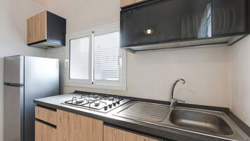 A modern kitchen with a stainless steel refrigerator, a gas stove, a sink, and wooden cabinets.