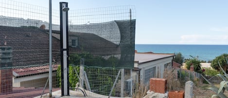 Un área cercada con una estructura de hormigón, un poste metálico y vista al mar.