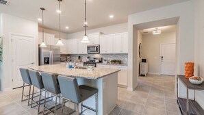 A modern kitchen with a large island, bar stools, stainless steel appliances, and pendant lighting. - 5BR Solterra Villa, Pool & Jacuzzi (Davenport)