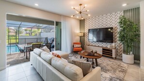 A modern living room with a large TV, comfortable seating, a dining area, and a view of a swimming pool. - 5BR Solterra Villa, Pool & Jacuzzi (Davenport)
