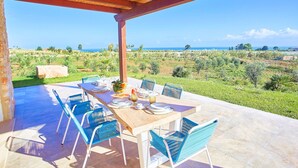 Een terras buiten met een houten pergola, een eettafel en stoelen.