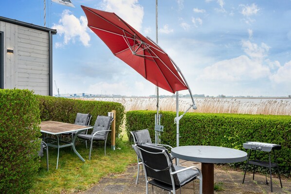 A patio with a table and chairs, a red umbrella, and a view of a water body. - Tiny House 'Ingo John Vanessa' with Sea View, Wi-Fi, and Air Conditioning (Sandstedt)