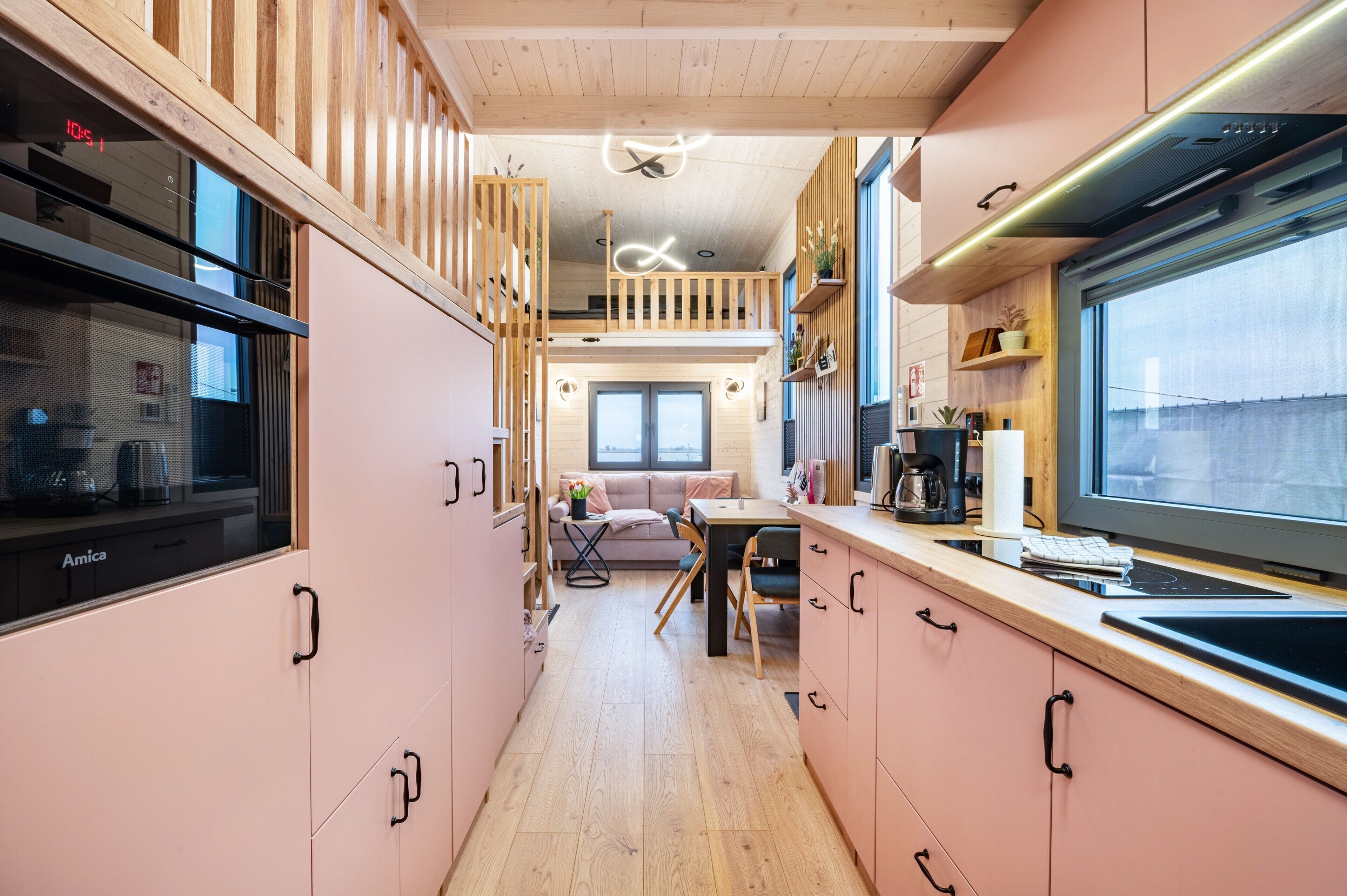 A compact kitchen with wooden cabinets, a dining area with a sofa, and a large window providing a view.