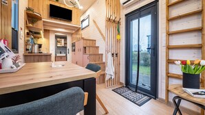 A modern kitchen with wooden cabinets, a dining table, and a TV mounted on the wall. - Tiny House 'Ingo John Vanessa' with Sea View, Wi-Fi, and Air Conditioning (Sandstedt)