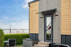 En modern byggnad med en träfasad, en dörr med ett glasparti och utsikt över en vattenyta.