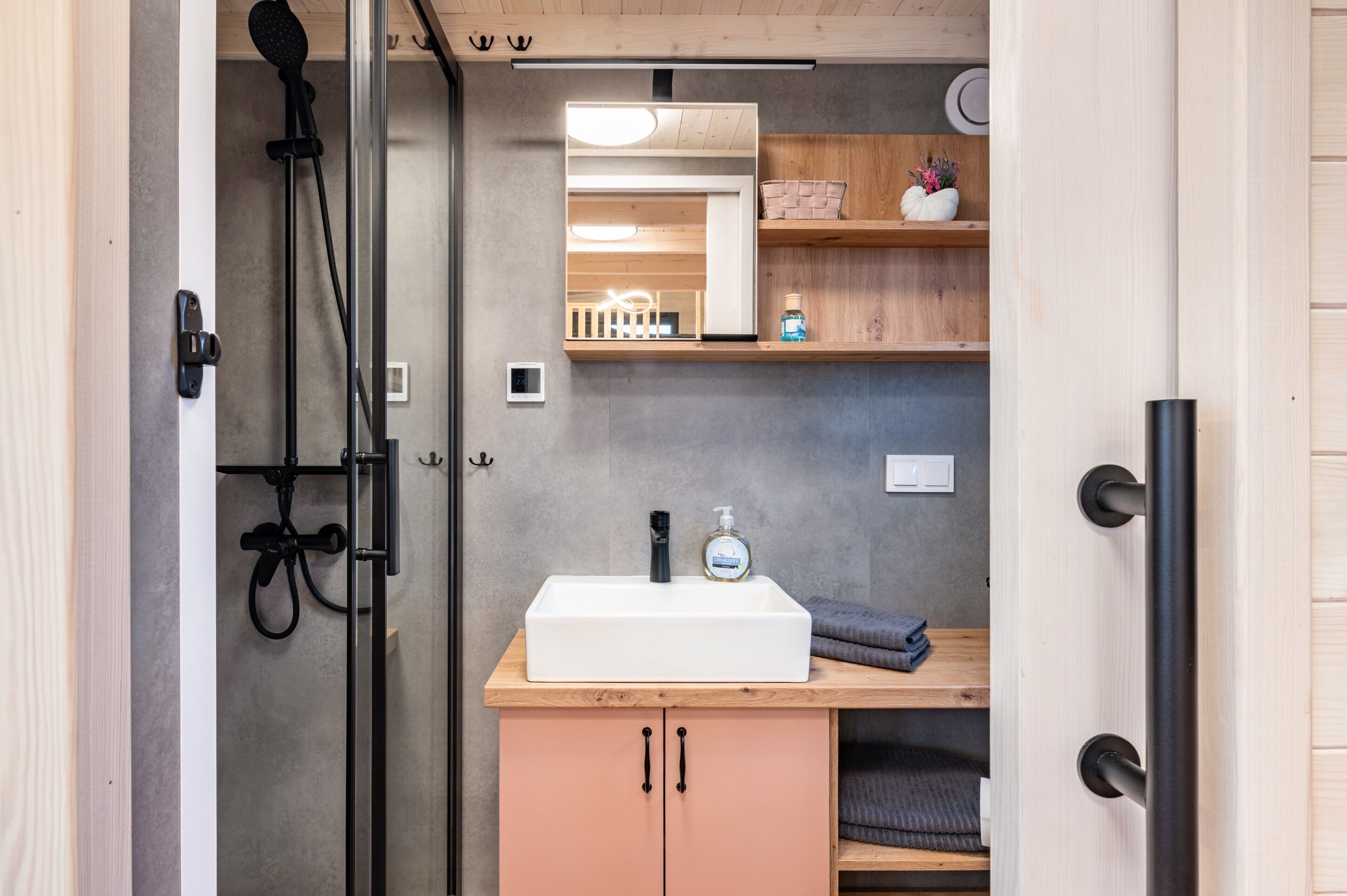 A bathroom with a white sink, wooden shelves, a mirror, and a shower area.