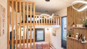A cozy room with a wooden slatted partition, a sofa, a small table, and a window. - Tiny House 'Ingo John Vanessa' with Sea View, Wi-Fi, and Air Conditioning (Sandstedt)
