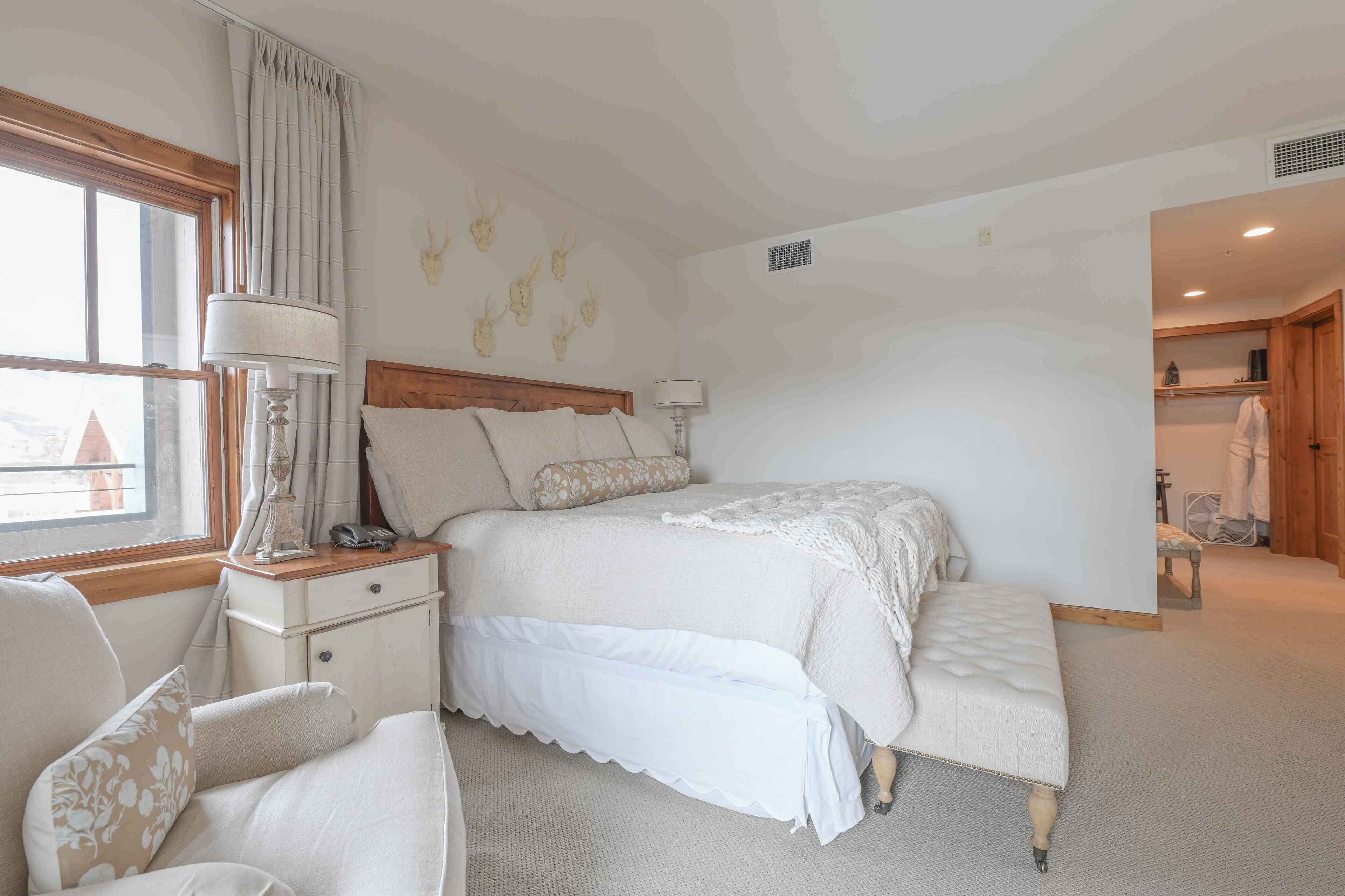 Une chambre à coucher avec un lit, une table de chevet, une lampe, une chaise et une fenêtre avec des rideaux.