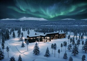 Um edifício moderno com várias janelas, cercado por uma floresta nevada e uma cordilheira ao fundo.