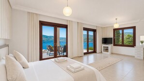 Una camera da letto con un letto, una televisione, un balcone con tavolo e sedie e vista sul mare.