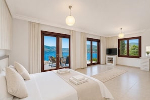 Un dormitori amb llit, televisió, un balcó amb taula i cadires, i vista al mar.