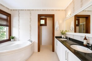 Ein modernes Badezimmer mit einer Badewanne, zwei Waschbecken, einem großen Spiegel und einer Topfpflanze.