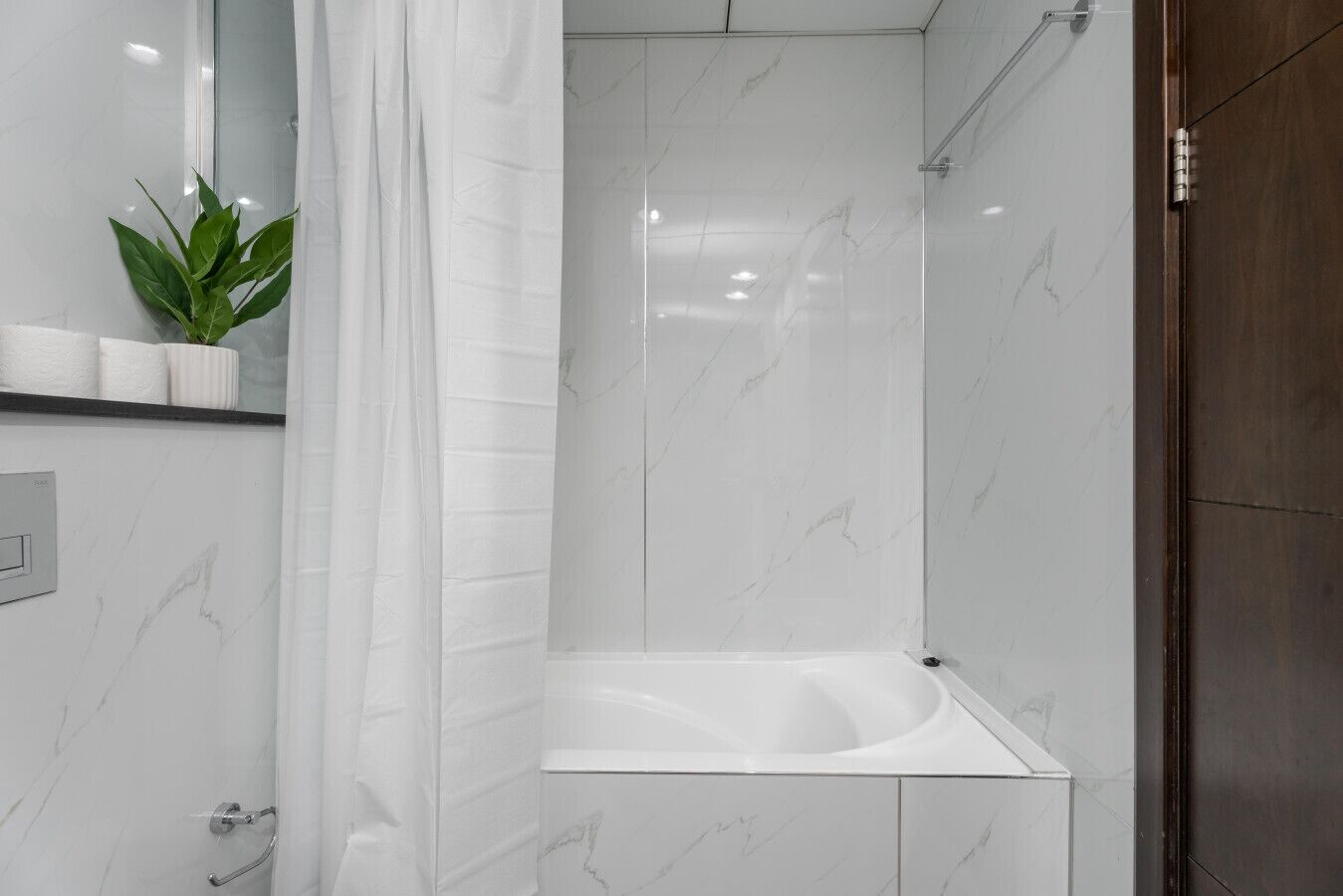 Ein modernes Badezimmer mit einer weißen Marmerdusche, einer integrierten Badewanne und einem Blumentopf auf der Ablagefläche.