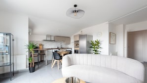 Ein modernes Wohnzimmer mit einer gebogenen Couch, einem Essbereich mit Tisch und Stühlen sowie einer Küche im Hintergrund.