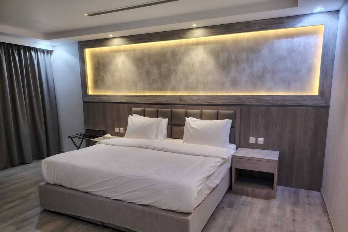 A modern hotel room with a large bed, bedside tables, and a wall-mounted light fixture.