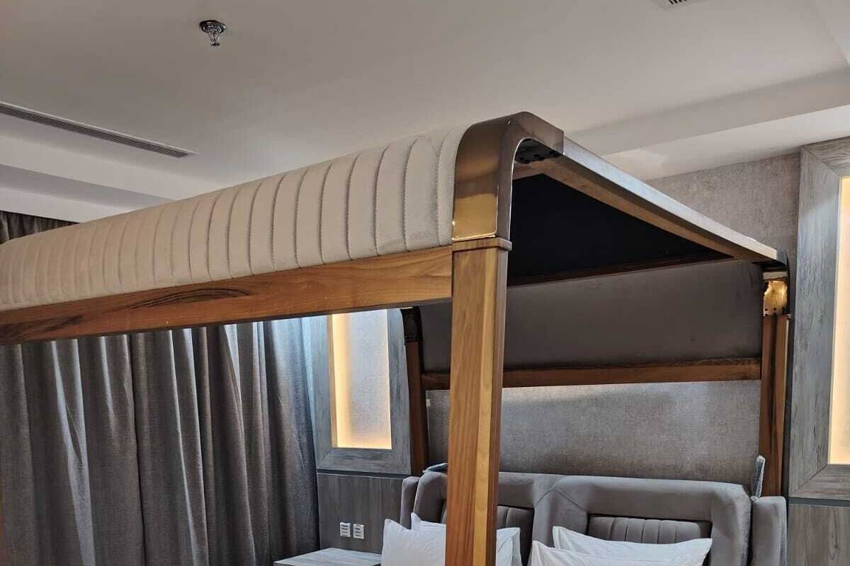 A four-poster bed with a wooden frame, grey upholstered headboard, and white bedding.