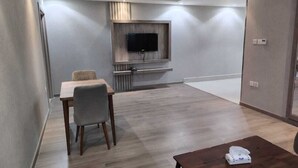A modern hotel room with a wooden floor, a dining table with two chairs, a flat-screen TV mounted on the wall, and a small table with a remote control. - HAYAT ROSE AL Madinah AL Munawwarah  (Madinah)