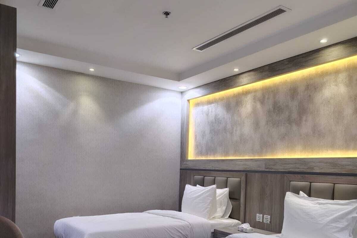 A hotel room with two beds, a small round table, and a modern headboard with integrated lighting.