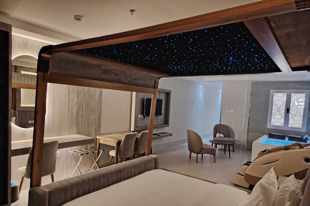A modern hotel room with a starry ceiling, a large bed, a desk, and a seating area.