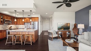 A modern kitchen with wooden cabinets, a central island with stools, stainless steel appliances, and pendant lighting. - New Listing 3 Bedroom on the Golf Course in sunny Poipu (Koloa)