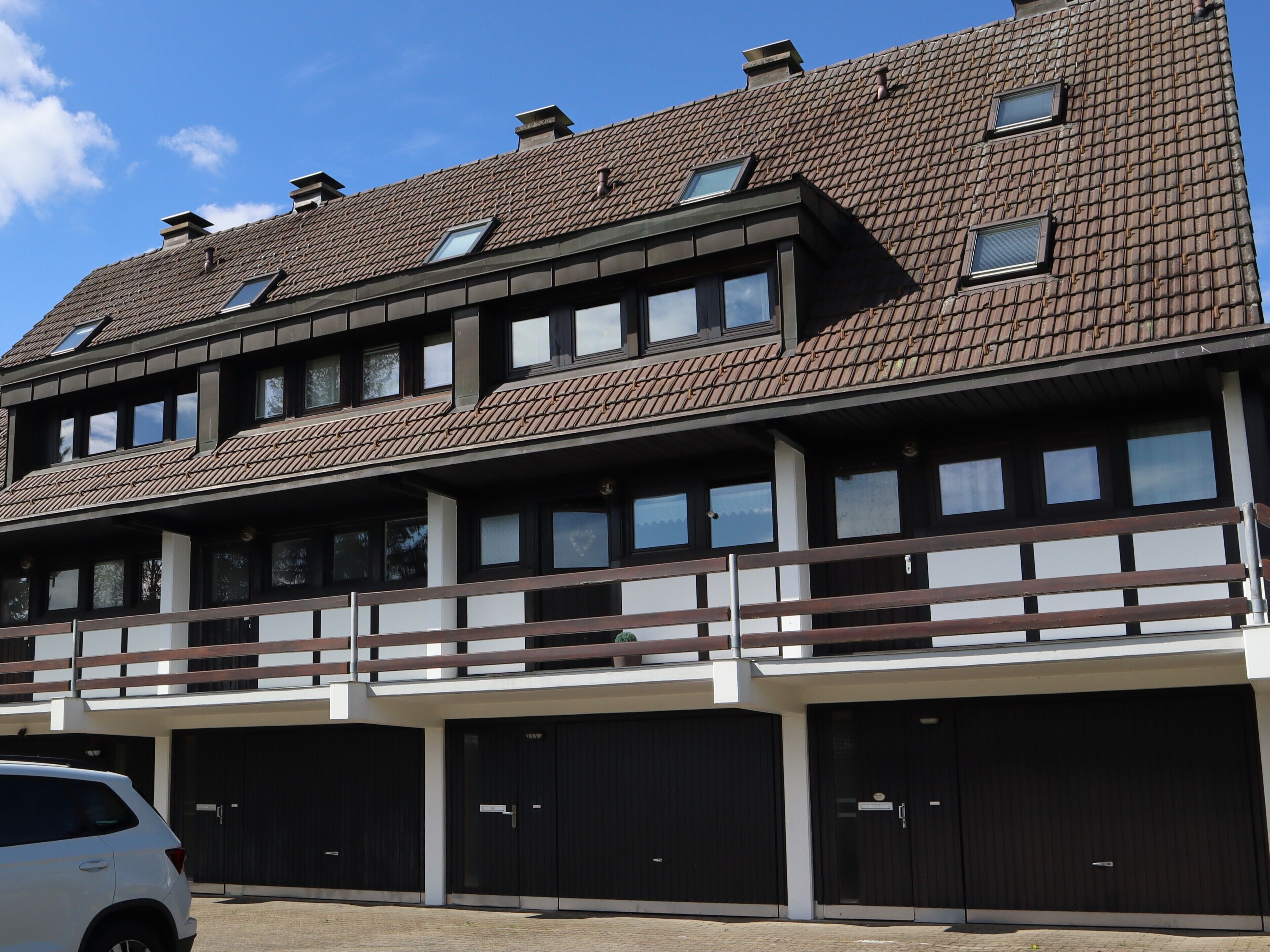 A multi-story building with a tiled roof, multiple windows, and a balcony. There are several garage doors visible.