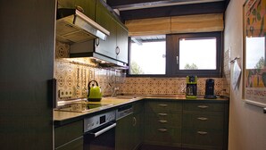 Una cuina amb rajoles decorades, una finestra i una tetera verda.