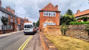 A street with a white van parked on the side, a brick building with a sign, and a brick wall with greenery. - Spacious & Luxury 2BR Flat in Calverton (Calverton)