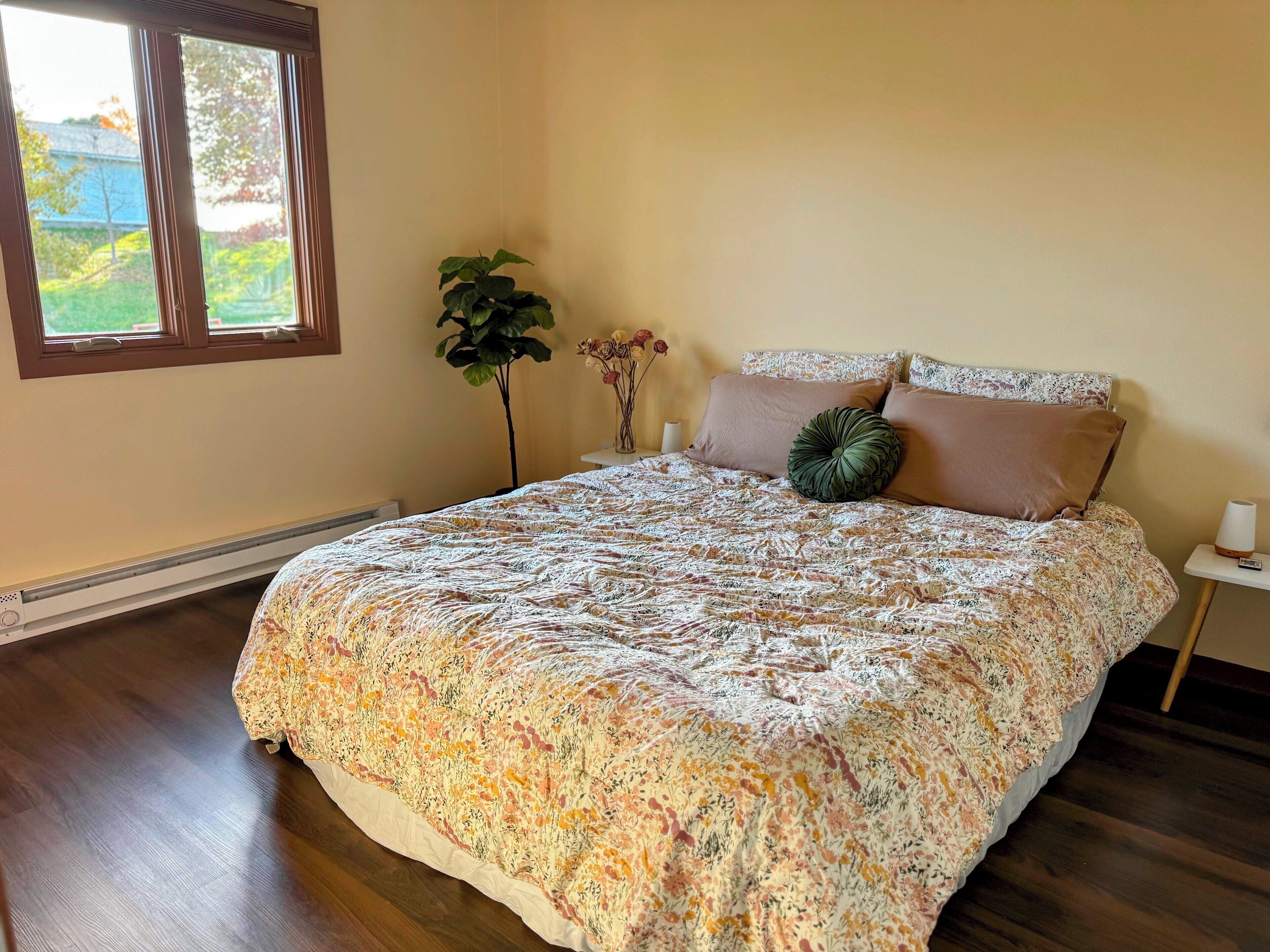 Une chambre à coucher avec une couvre-lit à motifs floraux, une plante en pot et un vase rempli de fleurs.