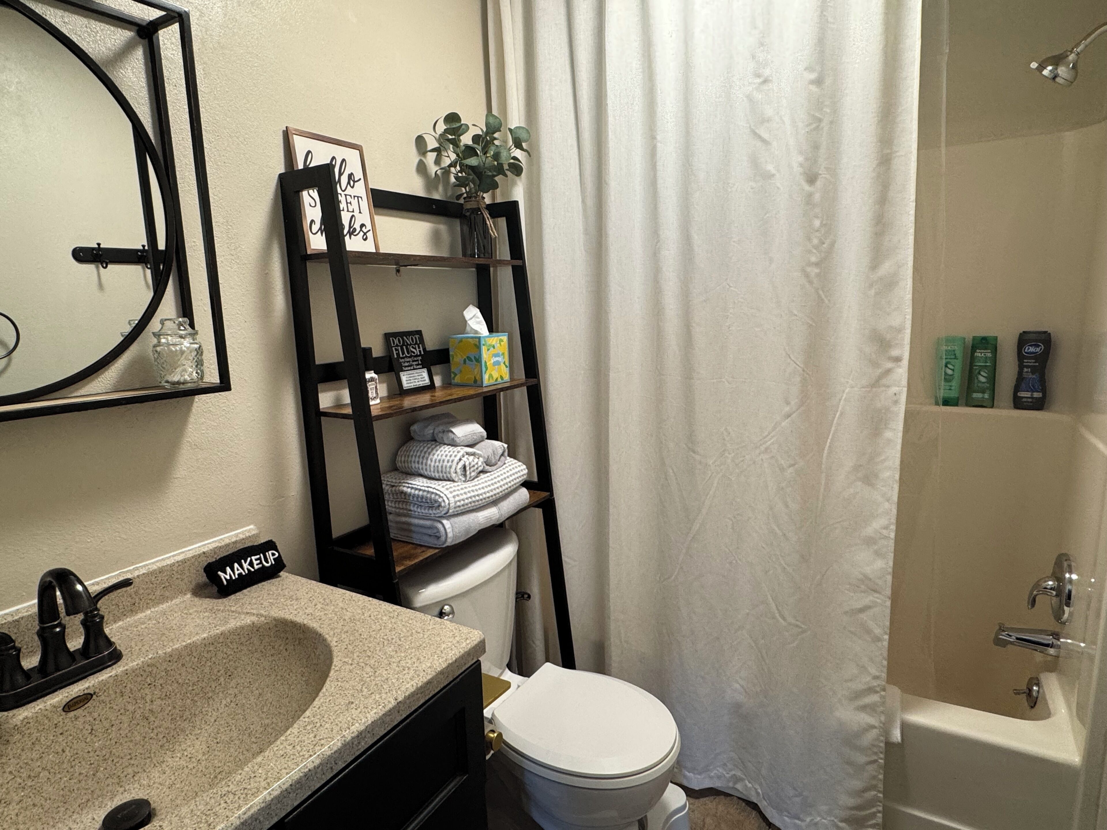 A bathroom with a sink, toilet, and shower. There is a shelf with towels and toiletries.