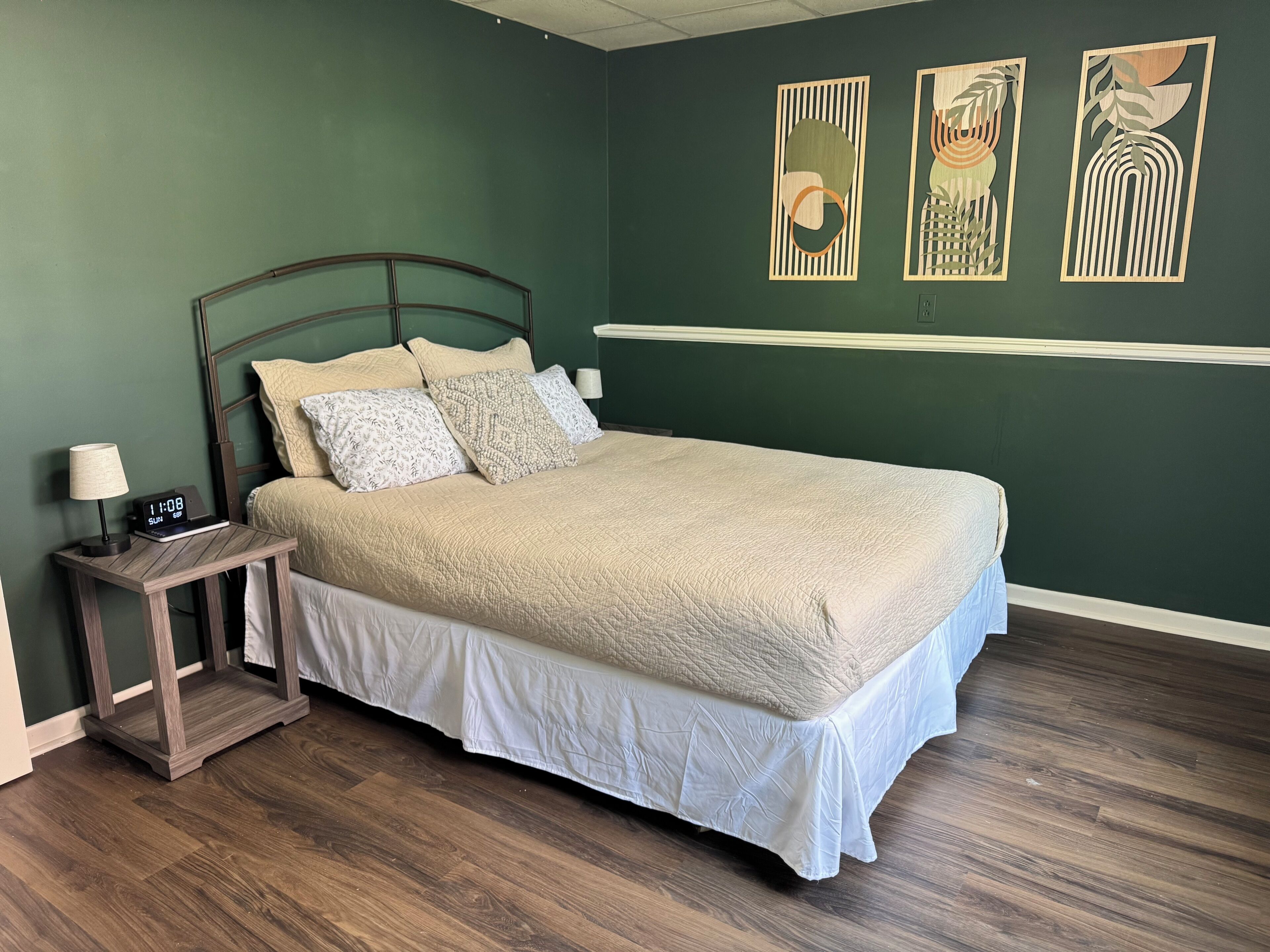 A neatly made bed with a white comforter and pillows, a bedside table with a lamp, and a wall clock.