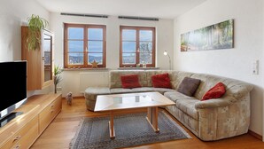 A living room with a sofa, TV, wooden cabinet, and a painting on the wall. - Apartment “Schellenberg” with Mountain View, Private Terrace, and Wi-Fi (Herrischried)