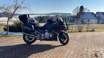 A black motorcycle parked on a paved surface with a rural landscape in the background.