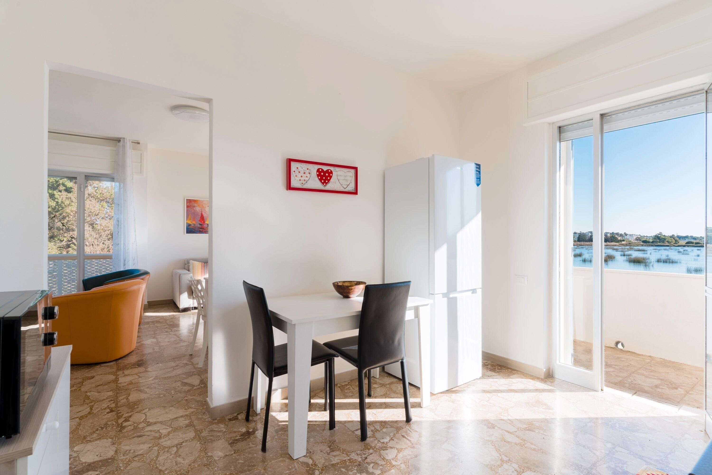 Eine moderne Küche mit einem weißen Tisch, schwarzen Stühlen, einem weißen Kühlschrank und Meerblick.