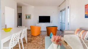 A living room with a flat-screen TV, white furniture, and a sofa with a patterned throw. - Holiday Home 'Rosso' with Private Terrace, Wi-Fi and Air Conditioning (Scala di Furno)