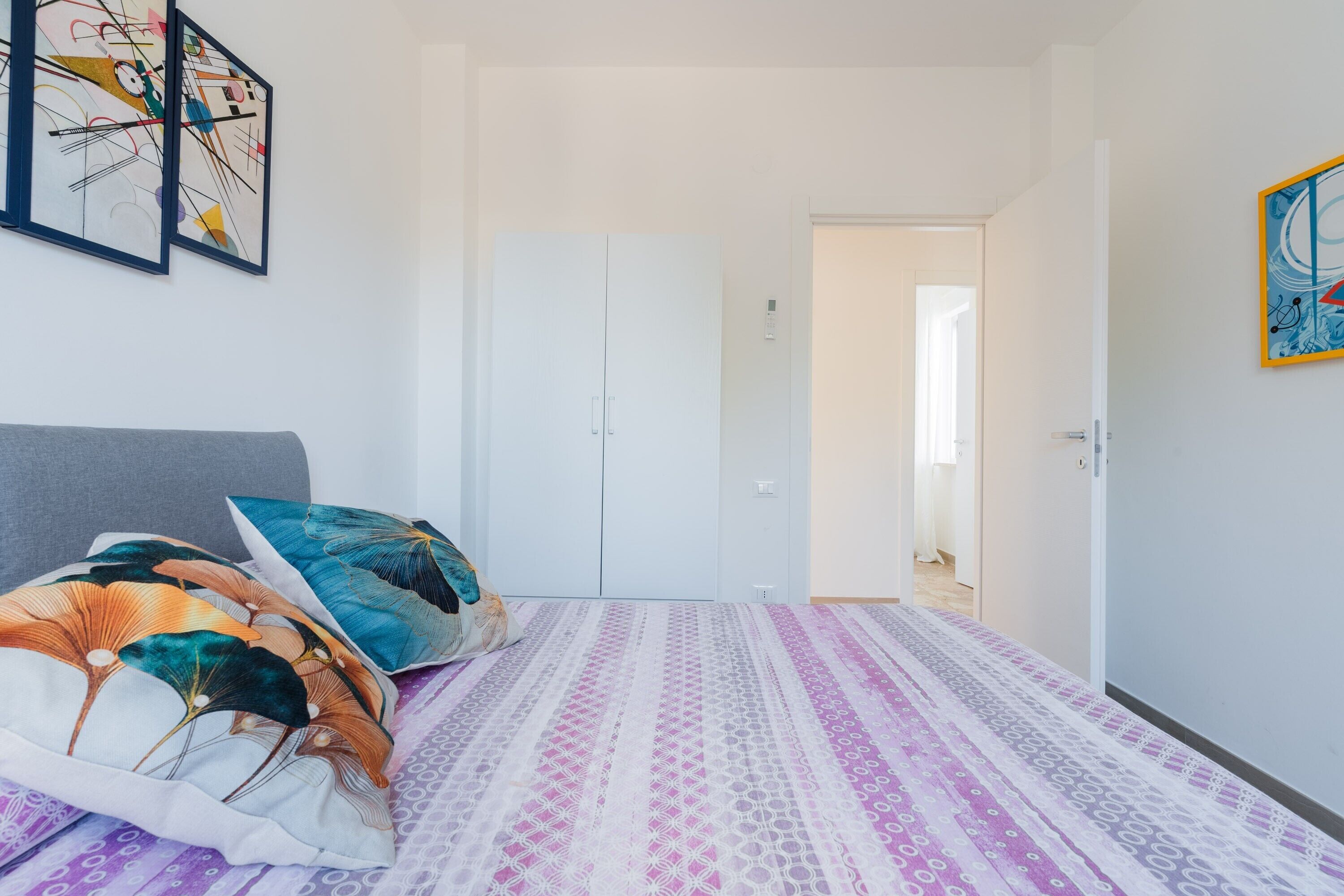 Ein Schlafzimmer mit Bett, Kissen, einem Kleiderschrank und einer Tür zu einem anderen Raum.