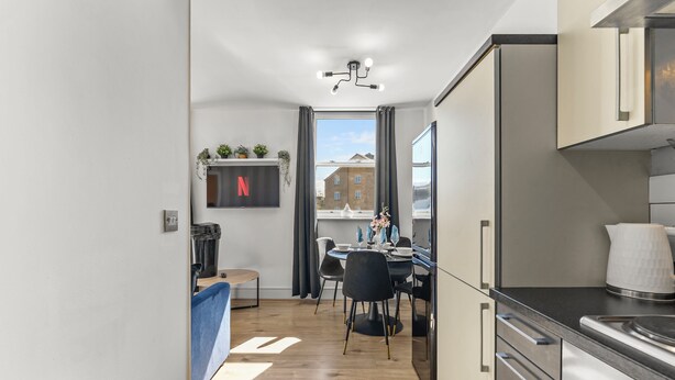 A modern kitchen with a dining area, a view of buildings outside, and a mounted Netflix logo. - Lovely Duplex for Long Stays - Parking (Dewsbury)