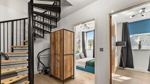 A modern interior with a spiral staircase, a wooden wardrobe, a bed with a blue headboard, and a view of the outside through a window. - Lovely Duplex for Long Stays - Parking (Dewsbury)