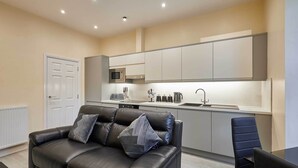 Uma sala de estar moderna com um sofá de couro preto, uma mesa de jantar e uma cozinha com armários brancos e um micro-ondas.