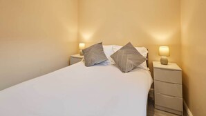 A neatly made bed with two pillows, a bedside table with a lamp, and a drawer unit. - Host & Stay | Ross's View, First Floor, Apartment 3 (Whitby)