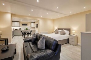 Una camera d'albergo moderna con un letto, una poltrona in pelle, una scrivania e angolo cottura.