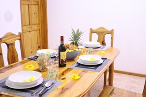 Une table de salle à manger en bois, mise avec des assiettes, une bouteille de vin, un panier de fruits et un ananas.