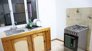 A compact kitchen with wooden cabinets, a stainless steel stove, and a window above the sink. - Sunset view suite personal Patio wiew panoramic mountain view and sunset (Trou D'eau Douce)