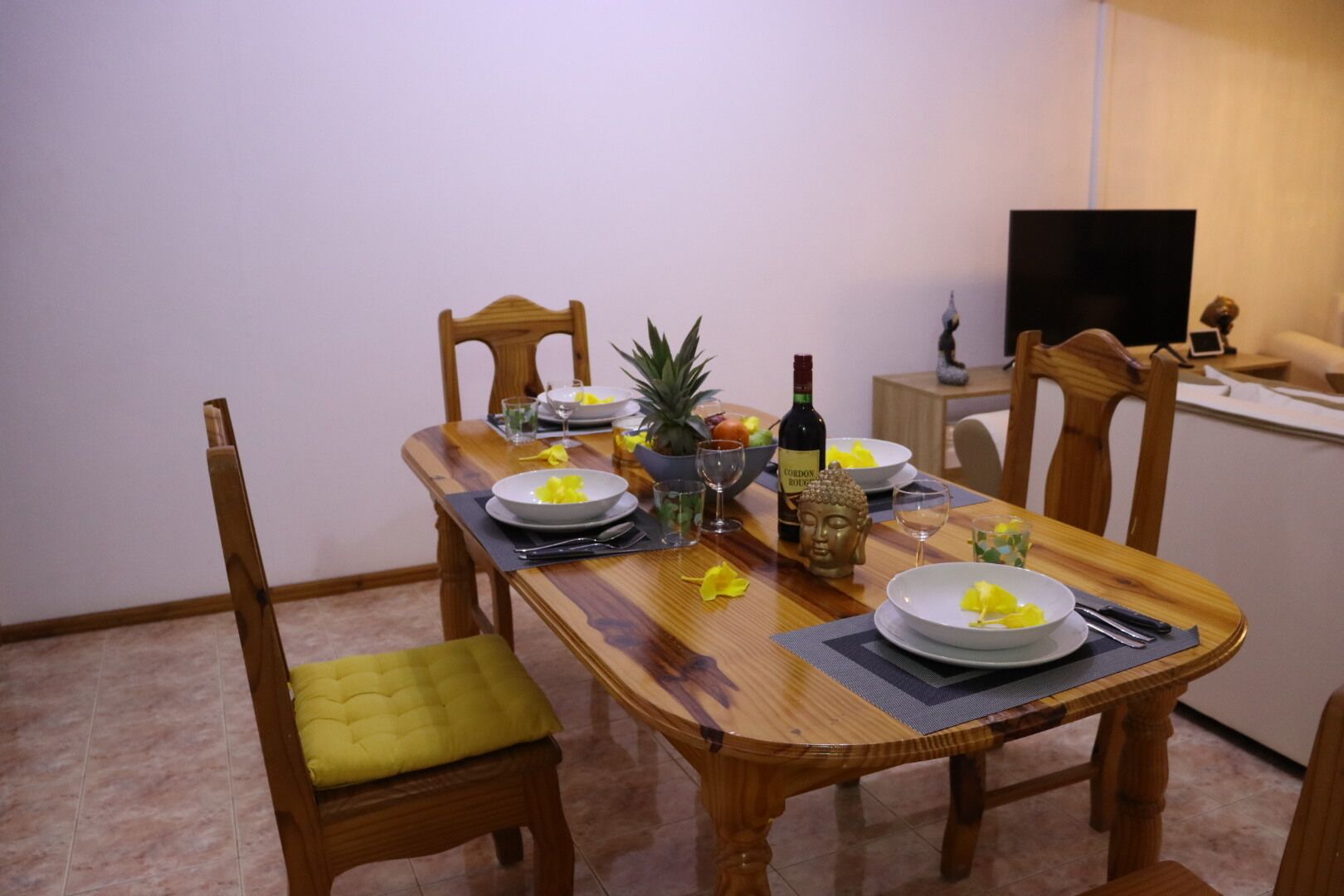 Een eettafel gedekt met borden, glazen en een fles, omringd door houten stoelen.